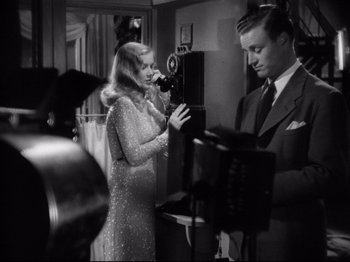 Movie still from “Hold Back the Dawn” (1941), directed by Mitchell Leisen – A man and a woman are standing in front of a camera; Medium shot, Low angle