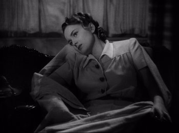 Movie still from “Hold Back the Dawn” (1941), directed by Mitchell Leisen – A woman sitting on top of a couch in a room; Medium shot, High angle