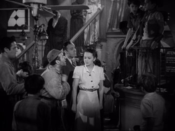 Movie still from “Hold Back the Dawn” (1941), directed by Mitchell Leisen – A group of people gathered around a woman; Medium shot, High angle