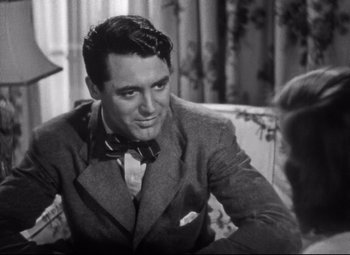 Movie still from “Holiday” (1938), directed by George Cukor – A man wearing a suit and a bow tie sitting on a couch; Close Up shot, Over the shoulder angle