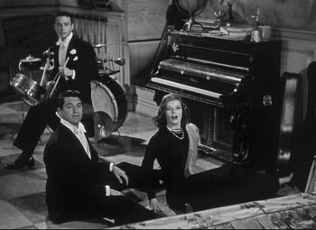 Movie still from “Holiday” (1938), directed by George Cukor – A black and white photo of a man and a woman singing; Wide shot, High angle