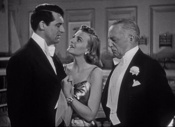 Movie still from “Holiday” (1938), directed by George Cukor – Two men and a woman in formal wear standing next to each other in a room; Medium shot, Low angle