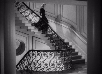 Movie still from “Holiday” (1938), directed by George Cukor – A black and white photo of a woman walking down a staircase; Wide shot, Low angle