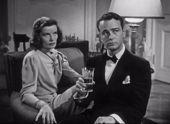 Movie still from “Holiday” (1938), directed by George Cukor – A man and a woman sitting next to each other holding drinks; Medium shot, Low angle