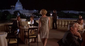 Movie still from “Hollow Man” (2000), directed by Paul Verhoeven – A woman in a silver dress standing in front of a table; Wide shot, Over the shoulder angle