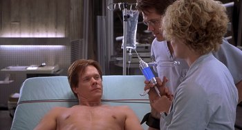 Movie still from “Hollow Man” (2000), directed by Paul Verhoeven – A man is lying in a hospital bed while two other men look on; Medium shot, High angle