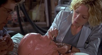 Movie still from “Hollow Man” (2000), directed by Paul Verhoeven – A woman is cutting a fake head with scissors; Close Up shot, Over the shoulder angle