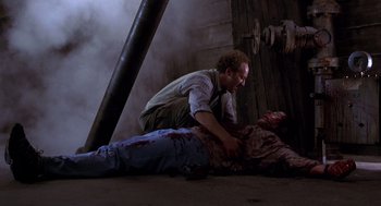 Movie still from “Hollow Man” (2000), directed by Paul Verhoeven – A man is laying on the ground with a dead man; Medium shot, Low angle