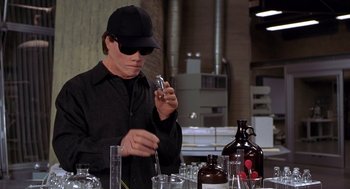 Movie still from “Hollow Man” (2000), directed by Paul Verhoeven – A man wearing a black hat and glasses looking at a cell phone; Medium shot, High angle