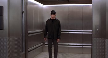 Movie still from “Hollow Man” (2000), directed by Paul Verhoeven – A man in a black shirt and black hat standing in an elevator; Wide shot, Low angle