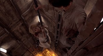 Movie still from “Hollow Man” (2000), directed by Paul Verhoeven – A woman hanging on a pole in a room with a man standing next to it; Wide shot, Overhead angle