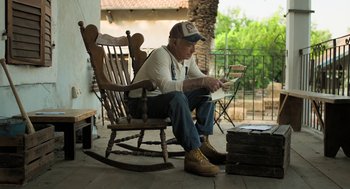 Movie still from “Holy Lands” (2017), directed by Amanda Sthers – An older man sitting in a rocking chair on a porch; Wide shot, Low angle