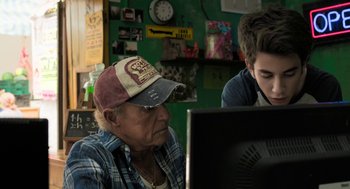Movie still from “Holy Lands” (2017), directed by Amanda Sthers – An older man and a young boy looking at a computer screen; Medium shot, Over the shoulder angle