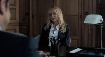 Movie still from “Holy Lands” (2017), directed by Amanda Sthers – A woman sitting in front of a table with a pair of scissors on it; Medium shot, Over the shoulder angle