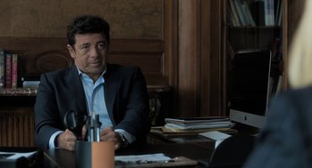 Movie still from “Holy Lands” (2017), directed by Amanda Sthers – A man sitting at a table in front of a bunch of books; Medium shot, Over the shoulder angle