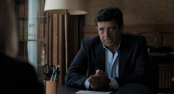 Movie still from “Holy Lands” (2017), directed by Amanda Sthers – A man sitting at a desk in front of a lamp; Medium shot, Over the shoulder angle