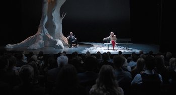 Movie still from “Holy Lands” (2017), directed by Amanda Sthers – Two people are sitting on a bench in front of an audience; Wide shot, High angle