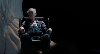 Movie still from “Holy Lands” (2017), directed by Amanda Sthers – An older man sitting in a chair with a laptop; Medium shot, High angle