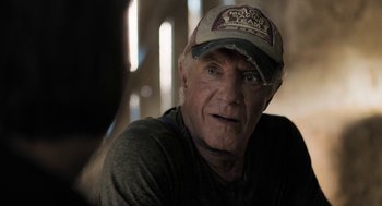 Movie still from “Holy Lands” (2017), directed by Amanda Sthers – An older man wearing a baseball cap and a gray shirt; Close Up shot, Over the shoulder angle
