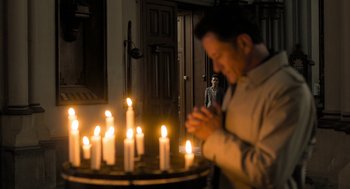 Movie still from “Holy Lands” (2017), directed by Amanda Sthers – A man standing in front of a table with candles; Wide shot, High angle
