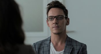 Movie still from “Holy Lands” (2017), directed by Amanda Sthers – A person wearing glasses and a jacket; Close Up shot, Over the shoulder angle