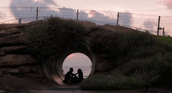 Movie still from “Holy Lands” (2017), directed by Amanda Sthers – Two people sitting in a tunnel next to the ocean; Wide shot, High angle