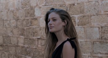 Movie still from “Holy Lands” (2017), directed by Amanda Sthers – A beautiful young lady standing in front of a brick wall; Close Up shot, Over the shoulder angle