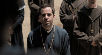 Movie still from “Holy Lands” (2017), directed by Amanda Sthers – A man wearing a black robe and a rosary; Close Up shot, Over the shoulder angle