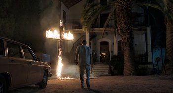 Movie still from “Holy Lands” (2017), directed by Amanda Sthers – A man standing in front of a burning cross; Wide shot, Low angle