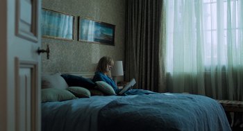 Movie still from “Holy Lands” (2017), directed by Amanda Sthers – A woman sitting on top of a bed reading a book; Wide shot, High angle