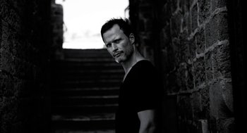 Movie still from “Holy Lands” (2017), directed by Amanda Sthers – A black and white photo of a man standing in front of some steps; Close Up shot, Low angle