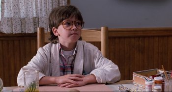 Movie still from “Honey, I Shrunk the Kids” (1989), directed by Joe Johnston – A young boy sitting at a table with his hands crossed; Medium shot, Low angle