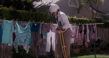 Movie still from “Honey, I Shrunk the Kids” (1989), directed by Joe Johnston – An older man wearing a helmet and holding a pair of crutches in a yard; Wide shot, Low angle