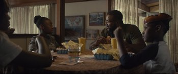 Movie still from “Us” (2019), directed by Jordan Peele – A man sitting at a table eating a sandwich; Medium shot, Over the shoulder angle