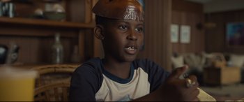 Movie still from “Us” (2019), directed by Jordan Peele – A young boy wearing a brown hat sitting in front of a laptop; Close Up shot, Low angle