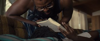 Movie still from “Us” (2019), directed by Jordan Peele – A man reading a book while lying on the ground; Close Up shot, Over the shoulder angle