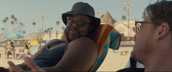 Movie still from “Us” (2019), directed by Jordan Peele – A man in a hat and sunglasses sitting on a beach chair; Close Up shot, Over the shoulder angle