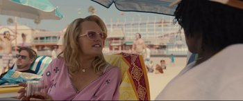 Movie still from “Us” (2019), directed by Jordan Peele – A woman in a pink dress and sunglasses on the beach; Medium shot, Over the shoulder angle