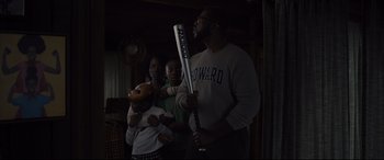 Movie still from “Us” (2019), directed by Jordan Peele – A man holding a baseball bat in a dark room; Medium shot, Low angle