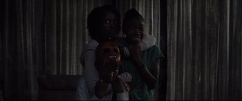 Movie still from “Us” (2019), directed by Jordan Peele – A group of people standing next to each other holding masks; Close Up shot, High angle