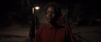 Movie still from “Us” (2019), directed by Jordan Peele – A person wearing a red shirt standing in a dark room; Close Up shot, Over the shoulder angle