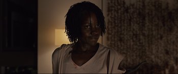 Movie still from “Us” (2019), directed by Jordan Peele – A young woman with long black dreadlocks wearing a white t - shirt; Close Up shot, Over the shoulder angle