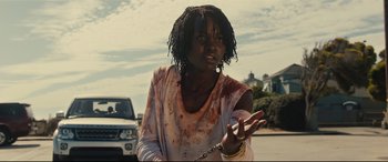 Movie still from “Us” (2019), directed by Jordan Peele – A young woman with dreadlocks is chained to the side of the road; Medium shot, Low angle