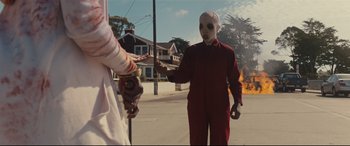 Movie still from “Us” (2019), directed by Jordan Peele – A person wearing a red suit and a mask; Medium shot, Over the shoulder angle
