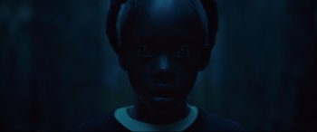 Movie still from “Us” (2019), directed by Jordan Peele – A young girl with dark hair and a black shirt; Close Up shot, High angle