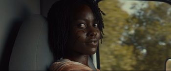 Movie still from “Us” (2019), directed by Jordan Peele – A young girl with black hair is sitting in a car; Close Up shot, Over the shoulder angle