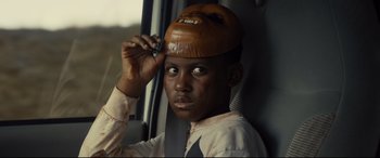 Movie still from “Us” (2019), directed by Jordan Peele – A young man with a wooden hat on his head is holding a cell phone to his head; Close Up shot, Over the shoulder angle