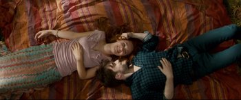 Movie still from “Horns” (2013), directed by Alexandre Aja – Two people laying on a bed smiling at the camera; Medium shot, Overhead angle