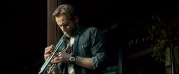 Movie still from “Horns” (2013), directed by Alexandre Aja – A man playing a trumpet in front of a building; Close Up shot, Low angle