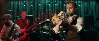 Movie still from “Horns” (2013), directed by Alexandre Aja – A man playing a trumpet in front of a microphone; Medium shot, Over the shoulder angle